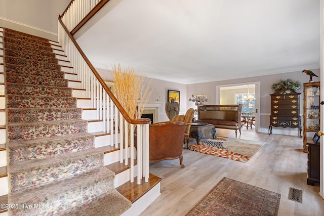 stairway with a fireplace, crown molding, visible vents, wood finished floors, and a chandelier