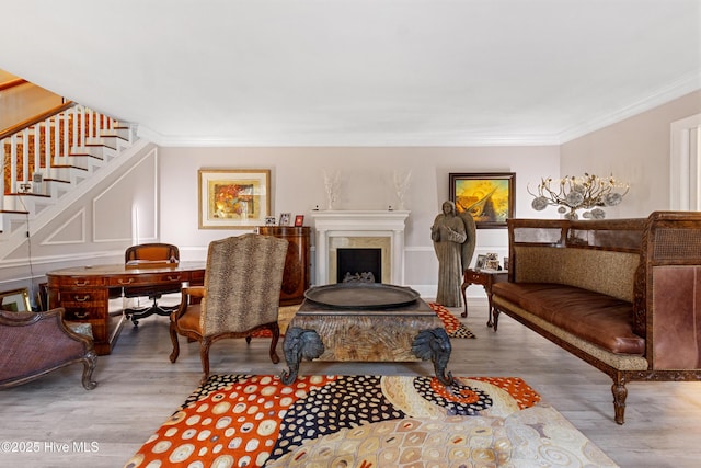 sitting room featuring a decorative wall, a fireplace, wood finished floors, stairway, and crown molding