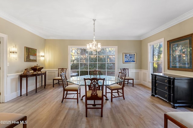 dining room with a chandelier, a wainscoted wall, ornamental molding, and light wood finished floors