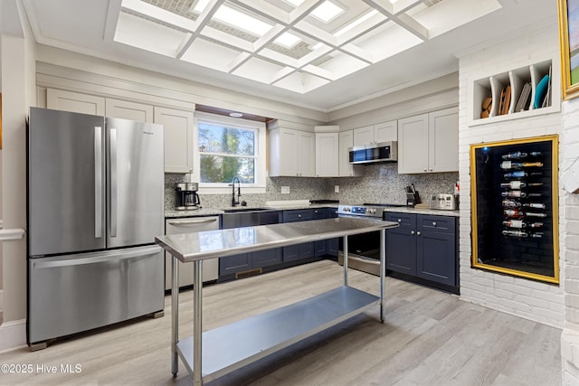 kitchen featuring light wood finished floors, stainless steel appliances, backsplash, a sink, and coffered ceiling