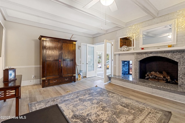 interior space with light wood-type flooring, ceiling fan, a fireplace with raised hearth, and beam ceiling