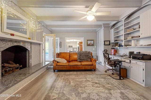 living area with a ceiling fan, beam ceiling, light wood-type flooring, a brick fireplace, and built in desk