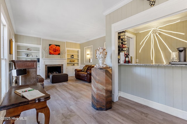 living area featuring built in features, baseboards, a premium fireplace, ornamental molding, and wood finished floors