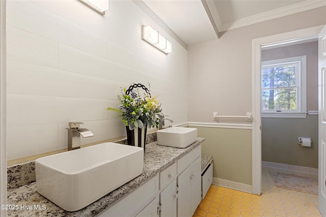 bathroom featuring double vanity, baseboards, ornamental molding, and a sink