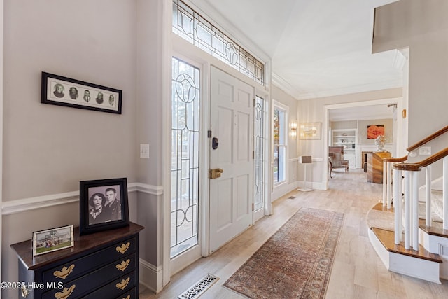 foyer with visible vents, baseboards, stairs, ornamental molding, and light wood-type flooring