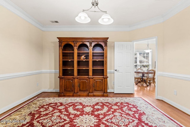 empty room featuring baseboards, visible vents, wood finished floors, crown molding, and a notable chandelier