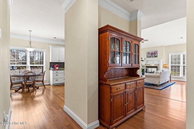 corridor featuring light wood-type flooring, baseboards, visible vents, and ornamental molding