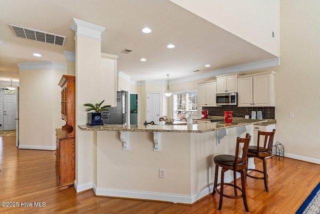 kitchen featuring visible vents, light wood-style flooring, appliances with stainless steel finishes, a breakfast bar, and a peninsula