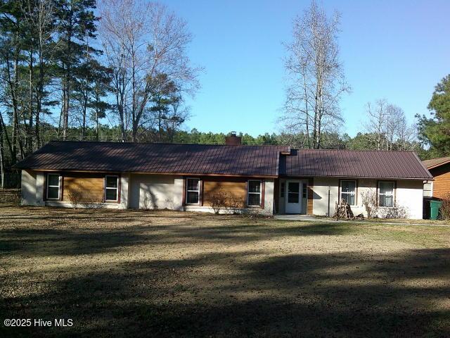 rear view of house with a chimney, metal roof, and a yard