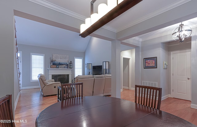 dining area with light wood-style flooring, a notable chandelier, a fireplace, baseboards, and crown molding