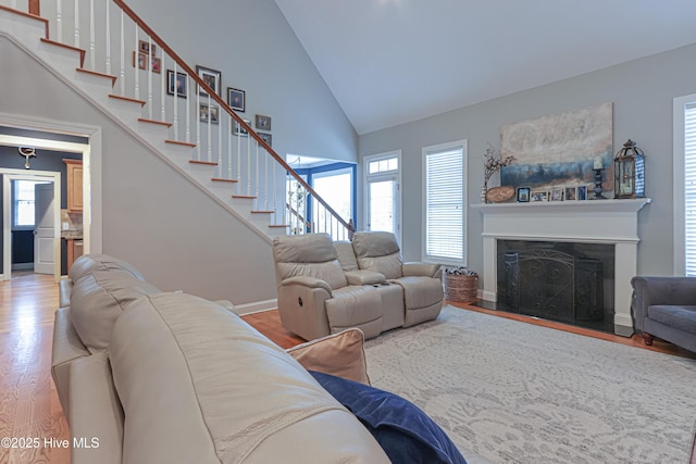 living area featuring a fireplace with flush hearth, plenty of natural light, stairway, and wood finished floors