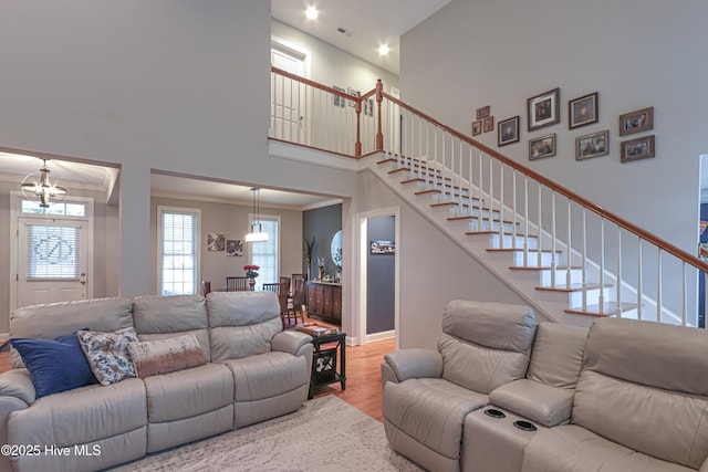 living area featuring visible vents, stairway, a high ceiling, ornamental molding, and wood finished floors