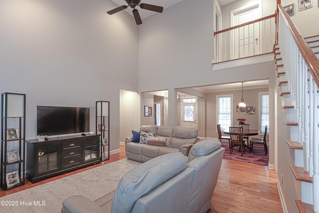 living room featuring a towering ceiling, ceiling fan, wood finished floors, baseboards, and stairs