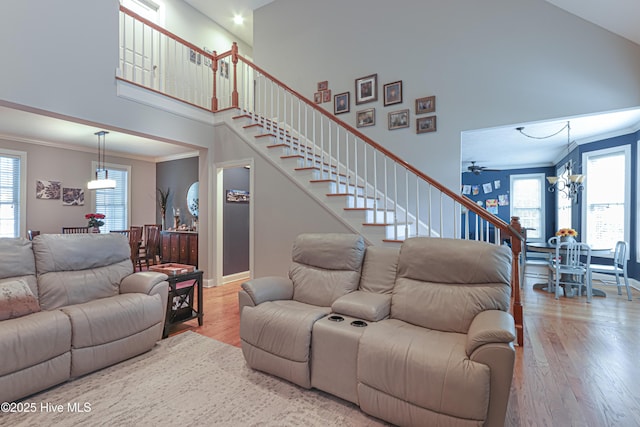 living room with a towering ceiling, stairs, ornamental molding, and wood finished floors