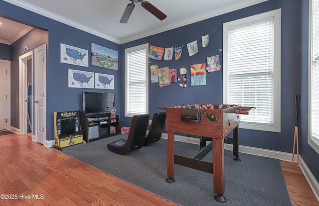 rec room with a ceiling fan, baseboards, ornamental molding, and wood finished floors