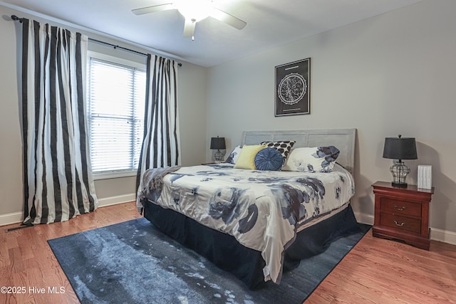 bedroom with a ceiling fan, visible vents, baseboards, and wood finished floors