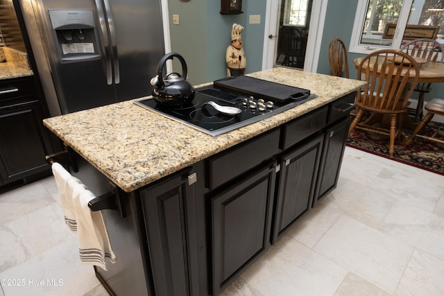 kitchen featuring a kitchen island, light stone counters, black electric stovetop, dark cabinetry, and refrigerator with ice dispenser