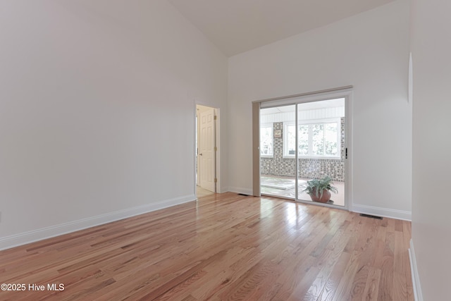 unfurnished room with a towering ceiling, visible vents, light wood-type flooring, and baseboards
