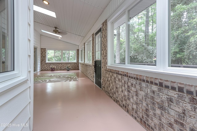 unfurnished sunroom with lofted ceiling with skylight, ceiling fan, and finished concrete floors