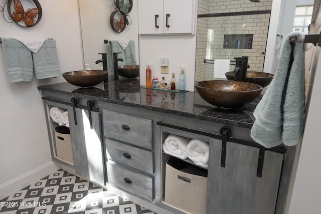 bathroom with tiled shower, a sink, baseboards, and double vanity