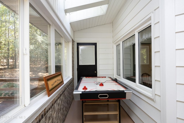 recreation room with vaulted ceiling with skylight and wood walls