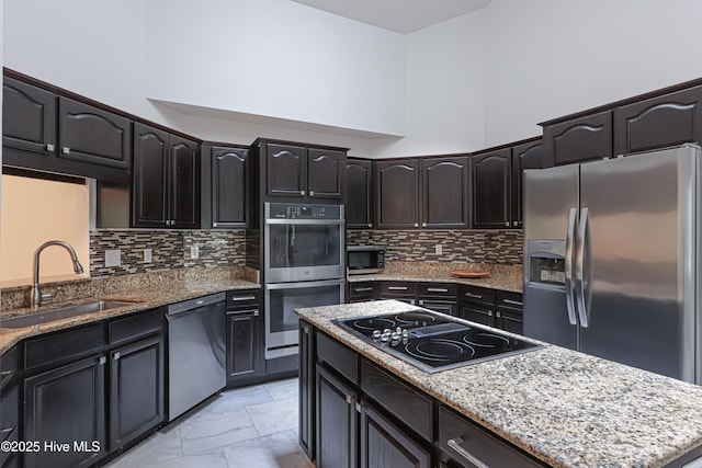 kitchen featuring light stone countertops, a sink, stainless steel appliances, and decorative backsplash