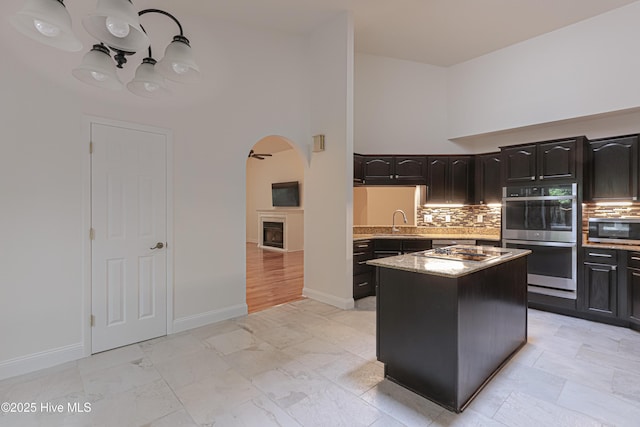 kitchen with arched walkways, decorative backsplash, appliances with stainless steel finishes, a sink, and a high ceiling
