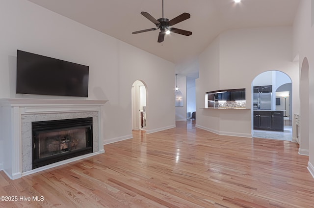 unfurnished living room featuring arched walkways, high vaulted ceiling, ceiling fan, and light wood-style flooring