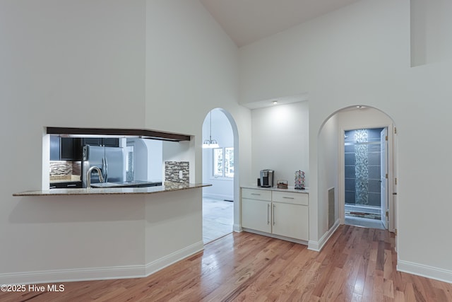 kitchen featuring light stone countertops, light wood finished floors, baseboards, high vaulted ceiling, and stainless steel refrigerator with ice dispenser