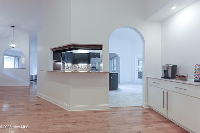 kitchen with a high ceiling, light wood-style floors, stainless steel fridge, arched walkways, and hanging light fixtures