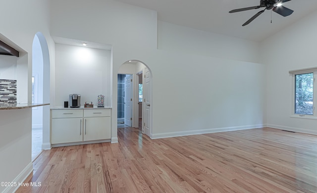interior space with visible vents, arched walkways, light wood finished floors, a ceiling fan, and high vaulted ceiling