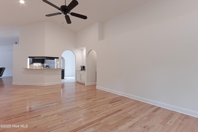 unfurnished living room featuring arched walkways, high vaulted ceiling, ceiling fan, and light wood-style floors