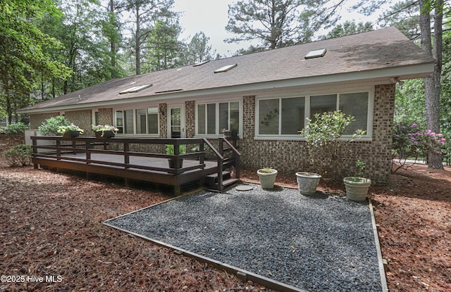 back of house with a deck, roof with shingles, and brick siding