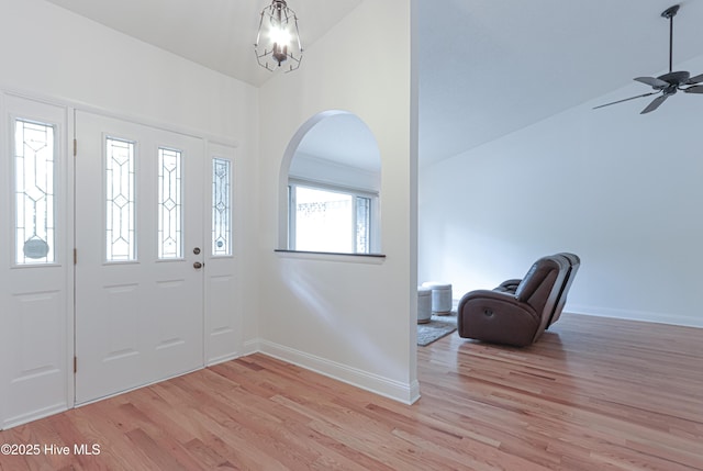 foyer entrance with baseboards, arched walkways, ceiling fan with notable chandelier, and light wood-style floors