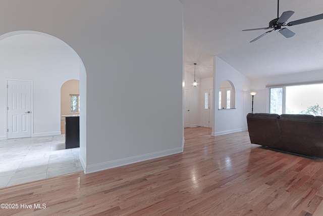 living area with arched walkways, ceiling fan, baseboards, light wood-type flooring, and lofted ceiling