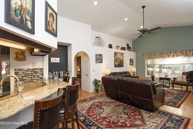 living room with arched walkways, ceiling fan, indoor wet bar, and wood finished floors