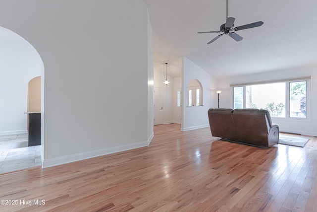 living area with arched walkways, baseboards, lofted ceiling, and light wood-type flooring