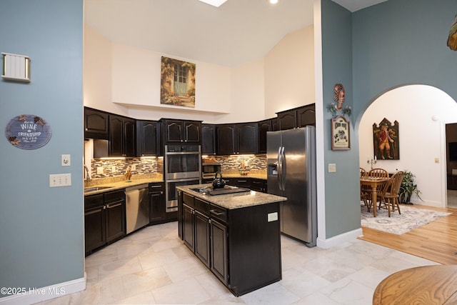 kitchen with arched walkways, a kitchen island, light stone counters, a high ceiling, and stainless steel appliances