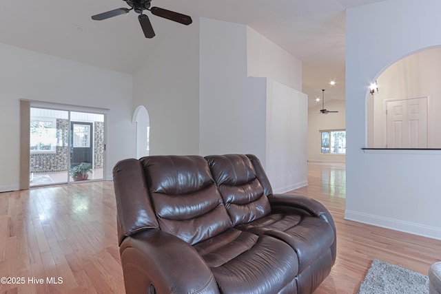 living room featuring arched walkways, ceiling fan, light wood finished floors, baseboards, and high vaulted ceiling