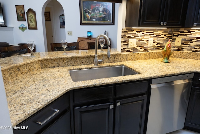 kitchen with arched walkways, decorative backsplash, light stone counters, stainless steel dishwasher, and a sink