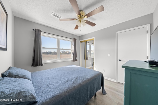 bedroom with visible vents, baseboards, a textured ceiling, and wood finished floors