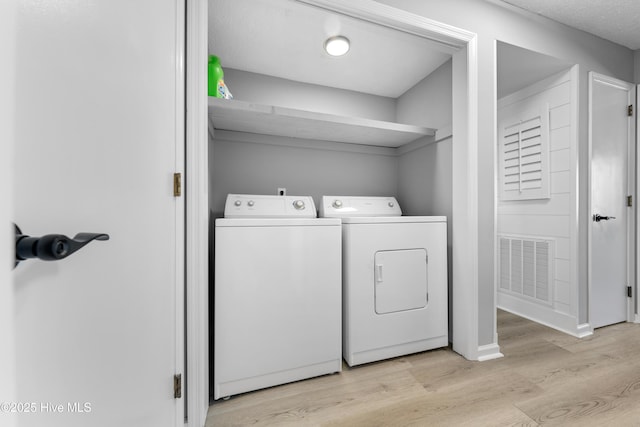 laundry area with laundry area, light wood-style floors, visible vents, and washer and clothes dryer