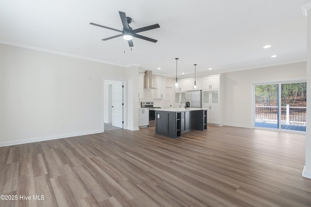 kitchen featuring white cabinets, appliances with stainless steel finishes, open floor plan, ornamental molding, and wall chimney range hood