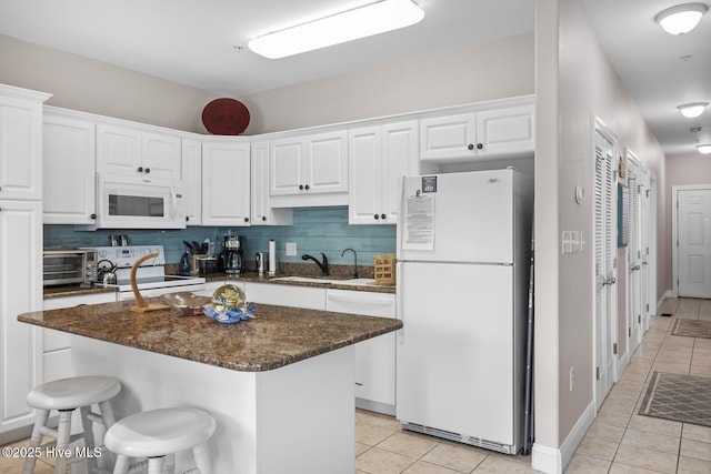 kitchen with light tile patterned floors, decorative backsplash, white cabinetry, a sink, and white appliances