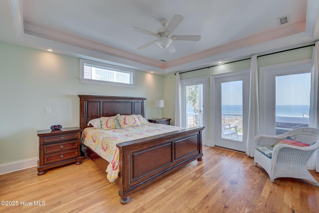 bedroom featuring access to exterior, a tray ceiling, visible vents, and light wood finished floors