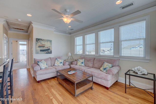 living room with attic access, visible vents, crown molding, and light wood finished floors