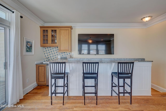 bar featuring baseboards, crown molding, light wood-style flooring, and decorative backsplash