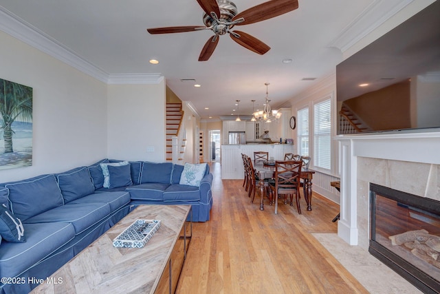 living area with crown molding, visible vents, light wood-style flooring, stairway, and a tiled fireplace