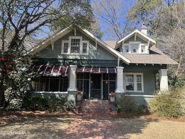 view of front of house featuring brick siding, a chimney, and a shingled roof