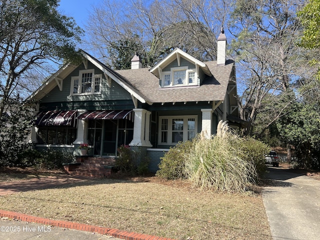 view of front facade with a shingled roof, brick siding, and a chimney